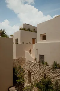A minimalist residential building with stucco walls, stone planters, and sparse landscaping.