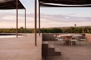 A modern outdoor lounge space with concrete flooring and furniture, surrounded by nature.