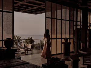 A woman standing in a modern hotel suite overlooking the ocean.
