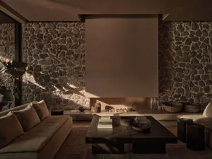 A modern living room with a stone wall, a wooden coffee table, and a large screen.