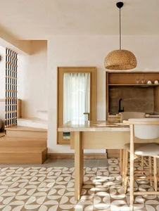 A modern kitchen featuring a cement floor with a geometric pattern, wooden dining table, and pendant light with a woven desig