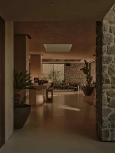 A modern living room with concrete flooring and walls, featuring a large stone fireplace and potted plants.