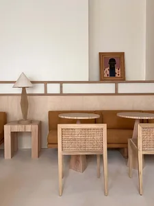 A minimalist room featuring modern wooden furniture with a round table, a square side table, and a lamp on a nightstand.