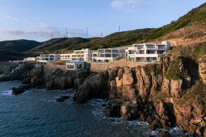 Modern residential architecture featuring stone, concrete, glass, and steel materials on a cliffside location.
