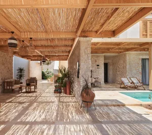 A wooden patio with a pergola structure, plants, and lounge furniture under a clear sky.