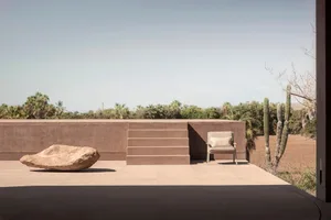 A minimalist landscape featuring a concrete structure, steps, and a single cushioned chair with a pillow.