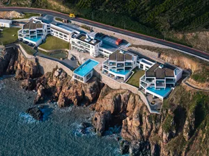Modern residential architecture with glass walls and a pool on a cliff overlooking the ocean.