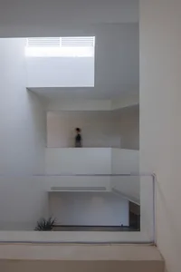 A minimalist, white, concrete architectural space with a person walking through it.