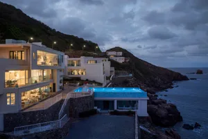 Modern residential building with concrete exterior and large glass windows overlooking the ocean.