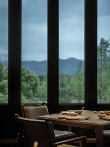 A modern restaurant interior featuring glass walls and wooden dining tables.