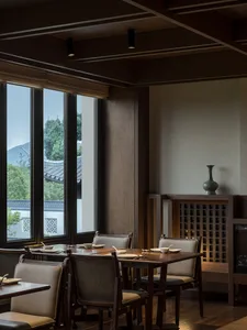 A modern restaurant interior featuring wooden tables and chairs, with large windows showcasing a scenic view of mountains and