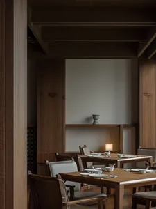 A modern restaurant interior featuring wooden tables and chairs, with a minimalist decor and soft lighting.