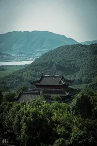一座傳統建築坐落於翠綠山丘與山巒之間，四周環繞樹木。