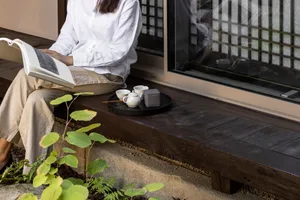 Person sitting on a wooden floor with a tea set and reading a book.