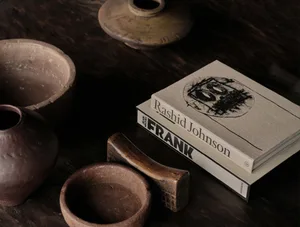 A photograph of rustic ceramic bowls and a book on Rashid Johnson's Frank, placed on a wooden coffee table.