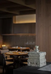 A stone pedestal with a small ceramic cup on top, set against the backdrop of an industrial-style restaurant interior with wo