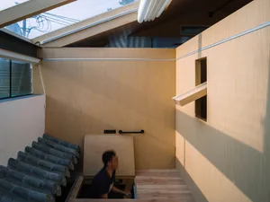 Minimalist architectural space with wooden walls and floors, featuring a skylight and a person entering through a door.
