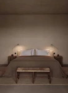 A minimalist bedroom featuring a bed with white pillows and a brown blanket, accompanied by two bedside lamps and a wooden be