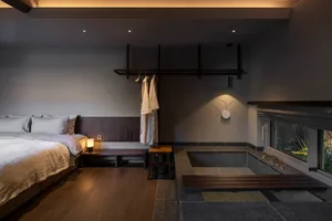 A minimalist bedroom featuring wood flooring, a stone bathtub, and a bed with textiles.