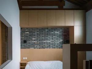 A minimalist bedroom with a wooden headboard and brick accent wall.
