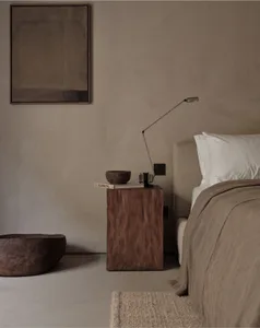 A minimalist bedroom featuring a wooden nightstand and bed, with a simple lamp and decorative bowls.