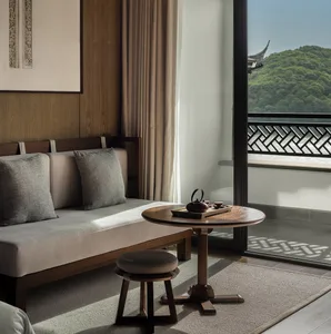 Spacious minimalist living room with light beige upholstered seating, wooden coffee table with tea set, and view of mountains