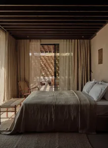 A bedroom with a simple, modern design featuring organic wooden furniture and light fabric textiles.