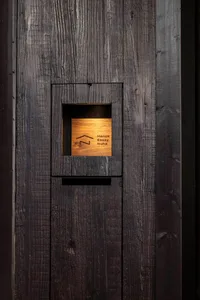 A close-up of a modern door detail featuring dark wood panels with a square cut-out containing branding information.