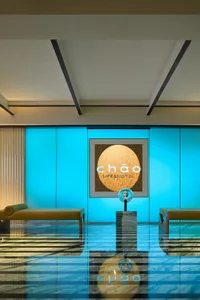 A modern hotel lobby featuring a blue backlit wall panel with a circular wooden logo display and two lounge chairs in front o