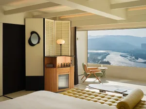 Modern hotel suite featuring neutral tones and minimalist design, with a large window overlooking mountains and a river.
