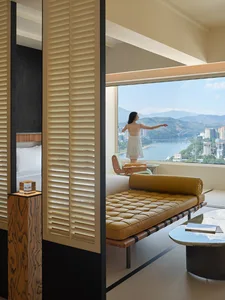 A modern minimalist residential interior with wooden furniture and a view of mountains and a cityscape from a large window.