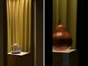 A glass pear sculpture on a wooden pedestal against a yellow curtain background.