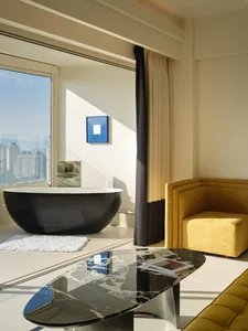 A modern suite bathroom featuring a black freestanding bathtub and a living area with a yellow armchair and coffee table.