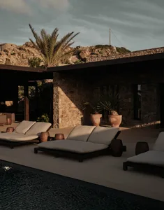 Outdoor deck of a resort villa with stone walls, concrete tiles, palm plants, and sun loungers.