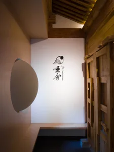 A minimalist wooden interior with a white circular light fixture and traditional Japanese calligraphy on the wall.