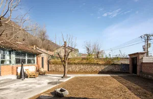 A traditional brick residential home with a stone wall and dry grass field.