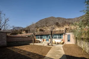 傳統磚造房屋搭配木質門廊與石牆，周圍是泥土地院與高大樹木。