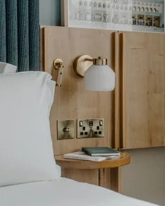 Minimalist bedroom featuring a wooden headboard and nightstand with books and a lamp.