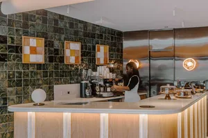 A modern coffee shop counter with a tiled wall, steel back panel, and wooden countertop.
