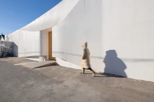 A person walking beside a modern, white, concrete exterior wall.