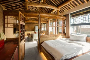 A modern industrial bedroom featuring a wooden bed frame, natural wood ceiling beams, and a white bed with a wooden headboard