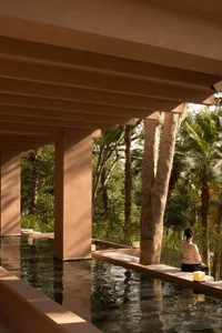 A modern outdoor space with concrete elements, a water feature, and a person relaxing on a bench.