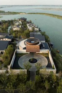 A modern waterfront house with a glass facade, wooden accents, and a circular roof structure.