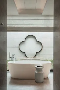 A modern bathroom featuring a white marble bathtub, a white marble pedestal, and a decorative quatrefoil mirror on the wall.
