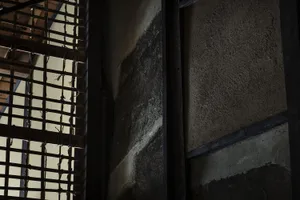 An ancient building interior view with a concrete wall featuring a window with a metal grille.