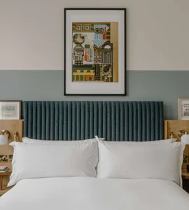 A modern bedroom with a blue pleated fabric headboard, white pillows, and a colorful abstract artwork