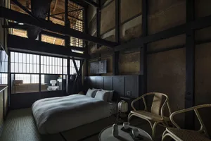 Minimalist bedroom featuring wood elements, with a large bed, two wicker chairs, and a low table in the foreground.