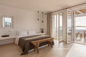 Minimalist bedroom featuring a wooden bed frame and wooden furniture, with a view of the sea through open glass doors.