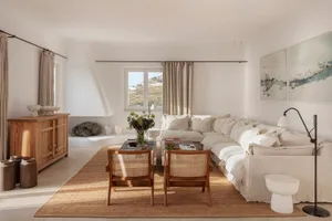 A modern minimalist living room with a large sectional sofa, wooden chairs, and a jute rug, featuring neutral-toned materials