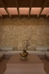 A minimalist living room with a stone wall and beige seating.